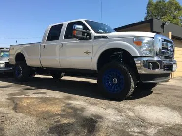 A white truck with blue tires parked in the street.