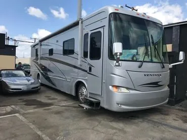 A silver rv parked in a parking lot next to two cars.